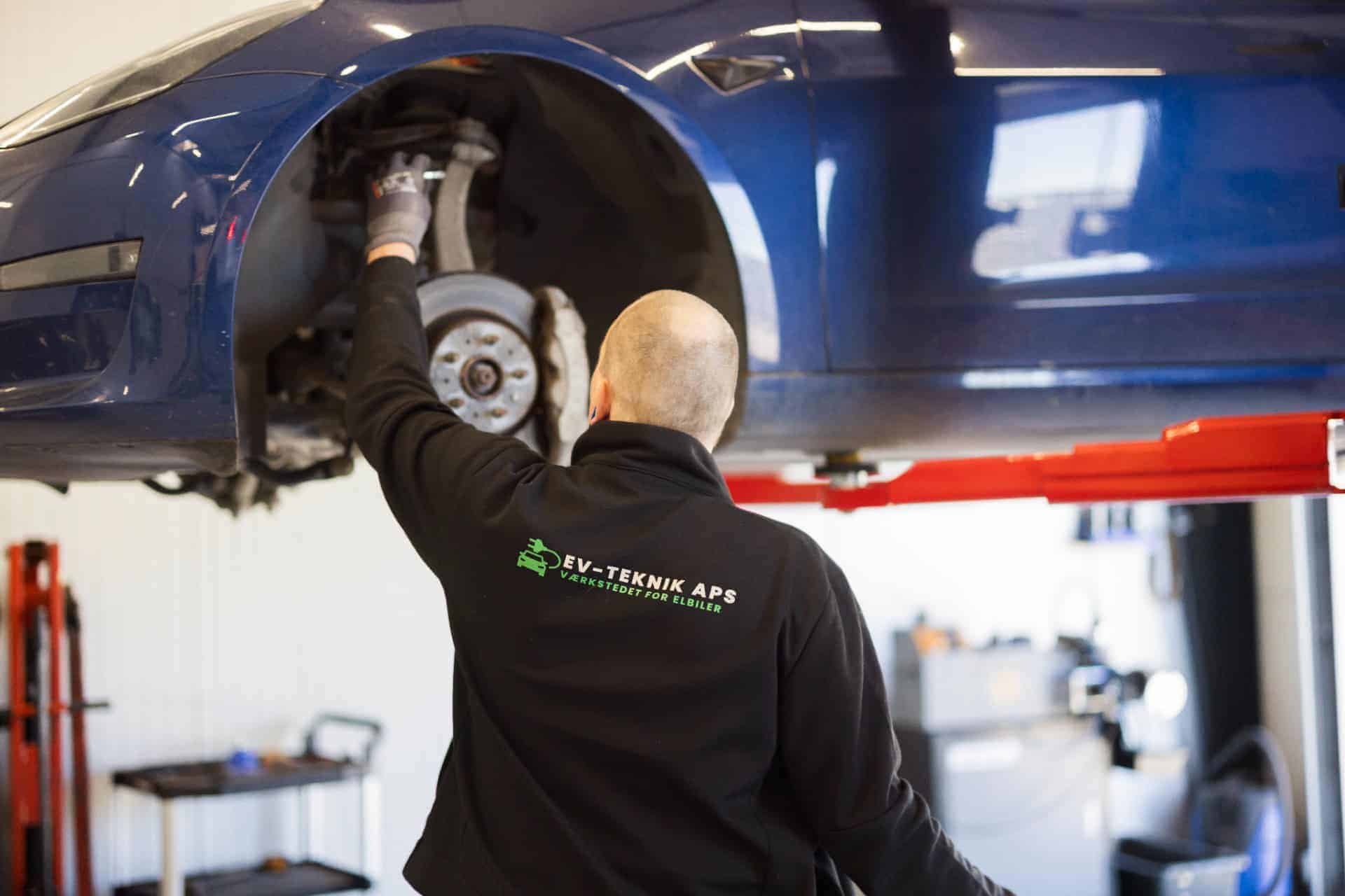 Mekaniker reparerer blå elbil nedefra på autolift - "EV-TEKNIK APS"