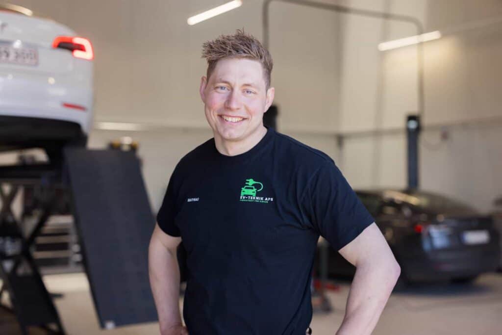 Nærbillede af smilende ung mekaniker under elbil reparation