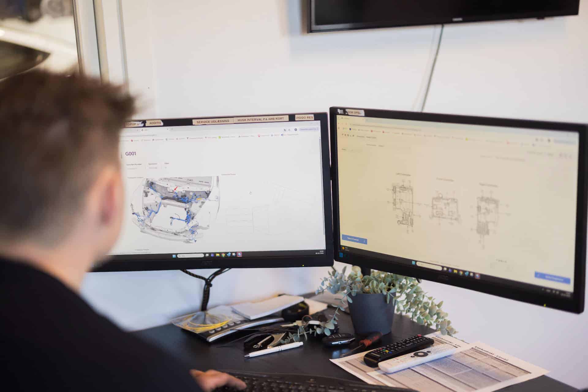 To computerskærme med tekniske tegninger til elbil service på værksted