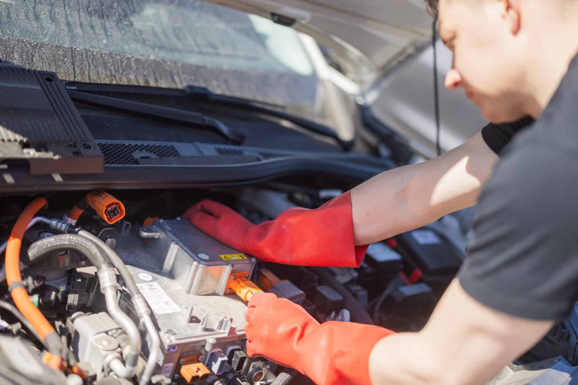 Mekaniker med røde handsker udfører elbil reparation i motorrummet